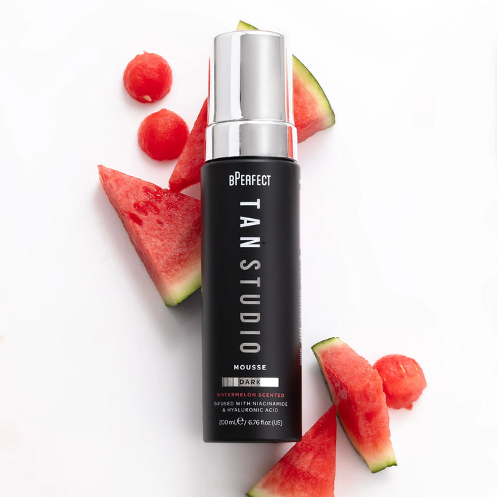 Black bottle of BPerfect Tan Studio Mousse with silver cap and watermelons on a white background